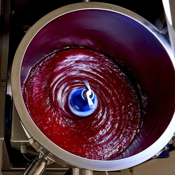 A top-down view of a large stainless steel vat containing a deep red liquid being stirred by a blue and white central agitator.