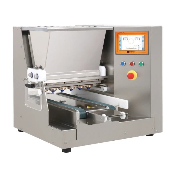 A stainless steel tabletop cookie depositing machine with a digital touch screen control panel, conveyor belt, and white mechanical arms, shown on a solid white background.