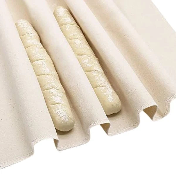 Two long bread loaves resting on a cream-colored bakers couche with soft folds and a plain white background.