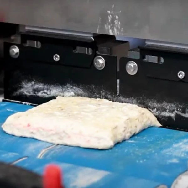 A rectangular piece of dough is being divided with an automatic cutter on a blue conveyor surface.