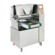 A stainless steel cookie depositor machine with a conveyor belt and touch screen control panel, mounted on a wheeled base with casters, shown against a plain white background.