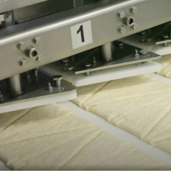 Close-up of the croissant-cutting section of a wholesale or industrial pastry line.