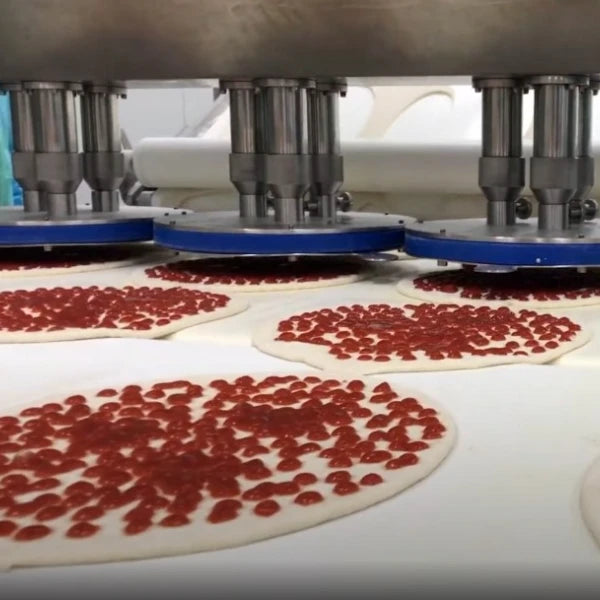 Pizza dough spread with red tomato sauce on a white conveyor belt under a pizza production line.