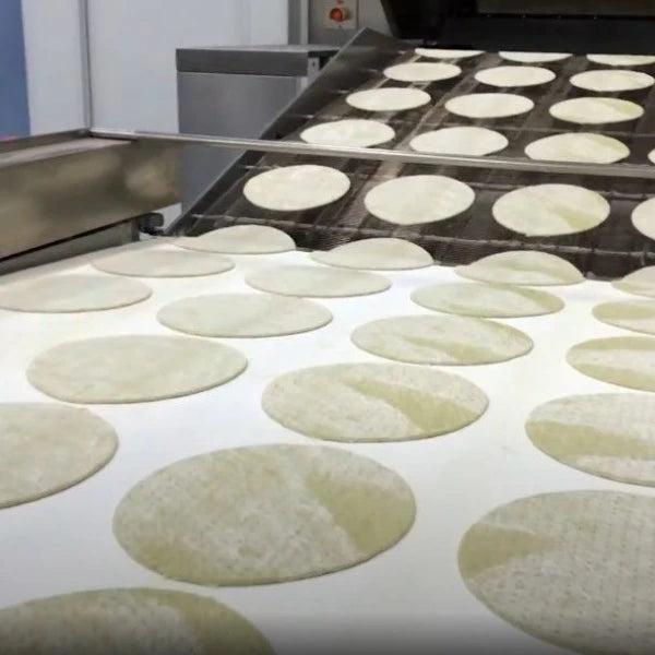 Pizza doughs are moving on a conveyor belt on a pizza processing line.